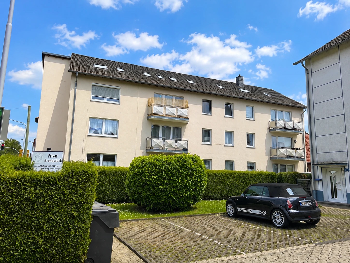 Beiges Mehrfamilienhaus mit Balkonen und gepflegter Hecke